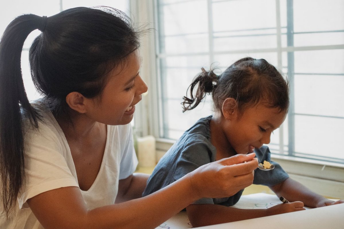 Mẹ đút cháo cho bé gái đang ngồi ăn ở bàn